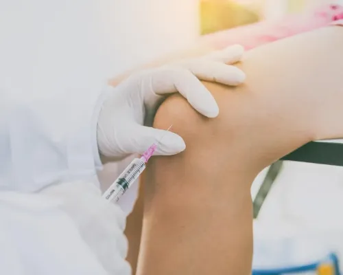 Gloved hands giving an injection into a patient knee